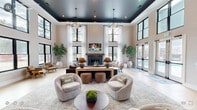 Located at 3500 Louis Stephens Dr in Durham, NC, this single-floor clubhouse delivers an impressive blend of modern design and comfortable communal living. The space is organized into two distinct living areas, each offering its own character while maintaining a cohesive aesthetic throughout.

The grand main lounge commands attention with dramatically soaring ceilings accented by a deep navy tray ceiling and statement geometric pendant chandeliers. Floor-to-ceiling black-framed windows flood the room with natural light, while sheer white drapery softens the space. A wood-mantled fireplace serves as a central focal point, flanked by plush seating arrangements and lush potted trees that add organic warmth. French doors open directly to a pool area beyond.

A striking set of black steel-framed sliding barn doors connects the lounge to a second, more relaxed living area. This room features light wood-look tile flooring, oversized framed landscape artwork, and curated seating arranged for casual gatherings.

The entry foyer sets the tone with patterned tile flooring, a sculptural round pedestal table, a circular halo chandelier, and an eclectic full-length mirror. A built-in refreshment bar with marble backsplash, gray cabinetry, and a coffee station is conveniently positioned near the main entrance, completing this well-appointed clubhouse.