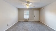 Located at 3430 Broad River Rd in Columbia, South Carolina, this efficiently designed single-floor unit offers a practical and functional layout. The kitchen is thoughtfully appointed with white laminate countertops, a coil-burner range, ample white cabinetry, and open wood-framed upper shelving that extends into a pass-through breakfast bar — creating a natural divide between the kitchen and the main living area. Hardwood-style vinyl flooring runs throughout the kitchen, providing a clean and easy-to-maintain surface. The living area features soft wall-to-wall carpeting, neutral beige walls, and a ceiling fan with integrated lighting, contributing to a comfortable and airy atmosphere. A window unit provides climate control, and a single window allows natural light to filter in, brightening the space. The textured ceilings are consistent throughout. The bathroom includes a clean, all-white tub and shower surround with a built-in shelf and towel bar, complemented by classic brass hardware. The overall design emphasizes practicality and efficient use of space, making it a well-suited option for those seeking a straightforward, low-maintenance living environment in Columbia, SC.