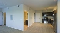 This single-floor residence offers a thoughtfully designed open-concept layout that seamlessly connects the main living areas. The space is finished with light-toned hardwood-style flooring that flows throughout the main areas, complemented by soft carpet in select zones, creating a warm and cohesive aesthetic.

The kitchen is a standout feature, equipped with stainless steel appliances including a range and built-in microwave, set against dark cabinetry with a tile backsplash. A ceiling fan with integrated lighting provides both comfort and illumination to the adjacent living space.

The open living and dining area benefits from a bright, airy atmosphere, thanks to neutral light-gray walls and multiple ceiling-mounted HVAC vents that ensure year-round comfort. The layout allows for flexible furniture arrangements, giving the space a versatile and functional character.

A bathroom is conveniently accessible from the main living area, featuring dark vanity cabinetry and a clean, functional design. A separate interior door provides access to additional private areas of the residence.

Overall, the space exudes a modern, minimalist ambiance with a neutral color palette, clean lines, and contemporary finishes that make it move-in ready and highly adaptable to a variety of interior styles.