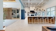 The Allure Apartments clubhouse at 450 Allure Cir in Whiteland, Indiana, is a thoughtfully designed community amenity space that blends modern aesthetics with a welcoming, social atmosphere. The single-floor layout offers a generous open-concept footprint, seamlessly connecting multiple activity zones within one cohesive environment.

The space is anchored by a striking bar-height counter with quartz surfaces and bar stool seating, accented by dramatic teardrop pendant lighting and a sculptural multi-arm chandelier overhead. A coffered ceiling with recessed lighting adds architectural depth throughout. Adjacent to the bar, a built-in fireplace with a wall-mounted television creates a comfortable focal point.

A dedicated game area features a pool table, shuffleboard, and an arcade gaming station set against a bold teal and navy accent wall bearing the Allure Apartments branding. A lounge zone offers plush seating arrangements for casual socializing, complemented by a beverage cooler stocked for residents' convenience.

Floor-to-ceiling sliding glass doors flood the space with natural light and open directly to an outdoor pool deck, creating a seamless indoor-outdoor connection. Contemporary artwork adorns the walls, and large-format light tile flooring runs throughout, tying the entire space together with a clean, polished finish.