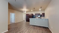 Located at 11206 University in Lubbock, Texas, this single-story space offers a well-designed open-concept floor plan that integrates the kitchen, dining, and living areas into one cohesive, functional layout. The kitchen is a standout feature, showcasing rich dark wood cabinetry, a light-toned countertop breakfast bar with decorative corbel supports, and pendant lighting that adds a warm, focused ambiance. Black appliances, including a refrigerator, range, and over-the-range microwave, provide a sleek, uniform look against the deep cabinetry. Recessed lighting throughout the ceiling complements the pendant fixtures, ensuring the space is well-lit. The floors are finished with wood-style planking that runs consistently throughout, adding warmth and visual continuity across the open layout. Neutral-toned walls create a clean, versatile backdrop suitable for a variety of interior styles. A chandelier anchors the living area, adding an elegant touch. The generous open floor plan allows for flexible furniture arrangement, making the space feel expansive and inviting. Doorways visible from the main area suggest additional rooms beyond, contributing to the overall functional design of this single-level property.