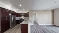 Located at 4826 Van Buren Blvd in Riverside, California, this single-story unit offers a thoughtfully designed layout with modern finishes throughout. The open-concept kitchen serves as the heart of the home, showcasing rich dark mahogany-toned cabinetry, granite countertops, and a full suite of stainless steel appliances including a gas range, microwave, dishwasher, and refrigerator. A peninsula countertop extends the workspace and creates a natural transition into the living area, which features durable wood-style plank flooring and recessed lighting. A bold red entry door adds a distinctive architectural accent to the main living space. The bedrooms are finished with plush carpeting and feature windows that invite natural light. The bathrooms are well-appointed with granite vanity countertops, dark wood cabinetry with brushed nickel hardware, and full tub-shower combinations with clean white tile surrounds. Wood-style flooring continues through the bathrooms, maintaining a cohesive aesthetic. Additional storage is provided by a tall pantry cabinet in the kitchen area. The overall design balances contemporary finishes with a warm, welcoming ambiance throughout the home.