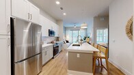 Located at 1464 Laurel Sound Ln in Sanford, FL, this thoughtfully designed one-bedroom, one-bathroom residence offers a smart, efficient layout that maximizes every square foot. The open-concept kitchen and living area serves as the heart of the home, anchored by a generous central island with a built-in sink and pendant lighting overhead. The kitchen is outfitted with white shaker cabinetry extending to the ceiling, a classic subway tile backsplash, stainless steel appliances including a French door refrigerator, microwave, and range, all set atop warm-toned hardwood-style flooring that flows throughout the space. The living area is bathed in natural light from large windows dressed with sheer curtains and wood blinds, creating a bright and airy atmosphere. The bedroom is a serene retreat, featuring large windows, soft neutral tones, and direct access to the spacious bathroom. The bathroom is elegantly appointed with a long dual-sink vanity, dark countertops, backlit mirrors, white cabinetry, and a floor-to-ceiling marble-tiled walk-in shower. A dedicated closet provides practical storage, completing this well-appointed Sanford residence.