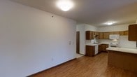 This two-floor residence offers a straightforward and functional layout designed for comfortable everyday living. The main living area is open and airy, featuring warm hardwood-style flooring that extends throughout the space, creating a cohesive and inviting atmosphere. Crisp white walls and flush ceiling lighting keep the interior feeling bright and clean.

The kitchen is positioned adjacent to the main living area and is well-equipped with warm-toned wooden cabinetry that provides generous storage space. Upper and lower cabinets line the walls, complemented by a double-basin sink, light countertops, and a built-in dishwasher. The kitchen's layout is efficient, making it practical for everyday meal preparation.

A doorway visible from the main area leads to additional spaces, contributing to the overall flow of the floor plan. The use of neutral tones throughout — from the white walls to the light flooring — creates a versatile backdrop that adapts easily to a variety of interior styles.

Spanning two floors, the residence offers separation between living and private spaces, providing both functionality and a sense of scale. The overall design is clean, practical, and well-maintained, making it a solid and dependable living space.