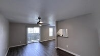 This single-floor residence offers a clean, modern aesthetic defined by a neutral gray color palette, crisp white baseboards, and textured ceilings throughout. The open living area is a standout feature, showcasing rich, dark hardwood-style flooring that extends seamlessly through the main living and dining spaces. A ceiling fan with integrated lighting adds both function and style, while a large sliding glass door floods the room with natural light and provides direct access to a private balcony with outdoor views. A secondary window further brightens the space. A convenient pass-through opening connects the living area to the kitchen, which is equipped with light-toned cabinetry and black appliances, creating a practical and visually cohesive workspace. The bedrooms offer a comfortable contrast with plush carpeting underfoot, ceiling fans, and windows with blinds that allow for adjustable natural light. Each bedroom includes generous closet space, with sliding mirrored-panel closet doors featured in one room. The overall ambiance of the residence is fresh, neutral, and move-in ready, with consistent finishes that create a cohesive and inviting environment throughout every room.