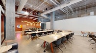 Located at 625 North 2nd Avenue in downtown Phoenix, Arizona, this contemporary office space offers a thoughtfully designed single-floor layout that balances open collaboration with private work environments. The space comprises 14 individual offices, two hallways, and a kitchen, all unified by a cohesive industrial-modern aesthetic.

The open work areas feature large communal tables with modern seating, exposed ductwork, and polished concrete floors that extend throughout the space. Soaring ceilings with open structural elements and concrete columns lend an airy, industrial character, while warm terracotta accent walls and a distinctive neon wavy light installation add visual energy to the collaborative zones.

Private offices and meeting rooms are enclosed with sleek black-framed glass partitions, maintaining visual connectivity while providing acoustic separation. Conference rooms are equipped with wood-tone tables, designer pendant lighting, and floor-to-ceiling windows that invite abundant natural light and views of the surrounding streetscape.

Lounge areas offer comfortable seating with sage green chairs, soft wall sconces, and potted greenery, providing welcoming spaces for informal gatherings. Well-lit hallways lined with glass-walled offices connect the various zones seamlessly. The kitchen and utility areas are finished in the same bold terracotta palette. Overall, the space strikes a refined balance between modern professionalism and creative warmth.