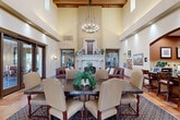 Located at 5082 N Primitivo Way in Fresno, CA, this single-floor community space showcases a refined Spanish Colonial architectural style that blends warmth and sophistication. The grand entrance foyer welcomes visitors with terracotta tile flooring, tall ceilings, and large glass doors that invite abundant natural light and views of the outdoor surroundings.

The main gathering area is defined by dramatically soaring ceilings adorned with exposed dark wood beams, creating an airy yet inviting atmosphere. A striking ornate fireplace with an elaborately carved stone surround serves as the room's focal point, flanked by comfortable leather sofas and upholstered seating arrangements. A large dining table with cushioned chairs occupies the central space, ideal for gatherings, beneath a wrought-iron chandelier.

A dedicated bar and kitchenette area, accessed through an arched opening, features dark granite countertops, warm wood cabinetry, tile backsplash, stainless steel appliances, and a wall-mounted television — offering all the amenities needed for events or daily use. A secondary kitchen area provides additional stainless steel appliances and ample cabinetry for storage. Wall sconces, recessed lighting, and carefully placed greenery complete the polished, welcoming ambiance throughout.