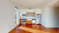 Located in Portland's vibrant Lower Buckman neighborhood, Unit 502 at 60 SE 10th Ave offers a thoughtfully designed single-floor layout with clean, contemporary finishes throughout. Rich hardwood flooring runs seamlessly through the main living areas, complemented by bright white walls that maximize the natural light pouring in through tall, floor-to-ceiling windows.

The open kitchen is a standout feature, equipped with stainless steel appliances including a gas range, built-in microwave, dishwasher, and full-size refrigerator. Warm wood cabinetry pairs with white upper cabinets and open wood shelving, while a classic white subway tile backsplash and a farmhouse-style sink add thoughtful design details. Track lighting above illuminates the workspace effectively.

A hallway with a sliding barn-style door connects to the bedroom, which is generously sized and bathed in natural light from a large corner window with outdoor views of the surrounding neighborhood. A ceiling fan adds comfort and functionality. The bedroom also features access to a dedicated walk-in closet complete with built-in shelving and in-unit laundry hookups.

The full bathroom is well-appointed with a soaking tub and shower combination, white cabinetry providing ample storage, and a dark-countered vanity. Clean, neutral finishes give the space a polished, functional feel throughout.