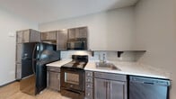 Located at 3080 E Cherry St in Springfield, Missouri, this one-bedroom, one-bathroom unit offers a smartly designed single-level layout that maximizes every square foot. The open-concept kitchen flows directly into the living area, creating a connected and functional living space. The kitchen is well-appointed with dark espresso cabinetry extending to the ceiling for generous storage, light-toned countertops, and a full suite of black Whirlpool appliances including a refrigerator, electric range, over-the-range microwave, and dishwasher. Light wood-style flooring runs throughout the main living areas, lending a clean and contemporary aesthetic. The living room receives natural light through a sliding glass door that opens to a private balcony, offering an outdoor retreat. The bedroom features neutral carpet, a window with blinds, and direct access to a dedicated closet. The bathroom is finished with wood-style flooring and includes a full tub-shower combination with a sliding glass enclosure. Additional utility and laundry rooms provide practical in-unit convenience. Recessed lighting and a neutral color palette throughout give the space a modern, move-in-ready feel.