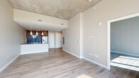 Located in the heart of Nashville at 805 Church Street, this modern 1-bedroom, 2-bathroom residence offers a sleek, contemporary design with impressive urban views. The open-concept living, dining, and kitchen area is anchored by light hardwood flooring and an exposed concrete ceiling that lends an industrial-chic character to the space. The kitchen is outfitted with stainless steel appliances, warm wood cabinetry, a tile backsplash, and a large island with a dark stone countertop and an integrated sink, illuminated by a trio of white pendant lights on a track rail system. The living area flows seamlessly toward floor-to-ceiling windows that frame sweeping panoramic views of the Nashville skyline, flooding the space with abundant natural light. The primary bedroom continues the airy aesthetic with soaring ceilings, exposed concrete detailing, and its own expansive window wall overlooking the city. The primary bathroom features large-format tile flooring, a dual-sink vanity with an illuminated mirror, and a glass-enclosed shower. Two closets and an in-unit laundry area add functional convenience, rounding out this well-appointed urban residence.