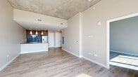 Located in the heart of Nashville at 805 Church Street, this modern 1-bedroom, 2-bathroom residence offers a sleek, contemporary design with impressive urban views. The open-concept living, dining, and kitchen area is anchored by light hardwood flooring and an exposed concrete ceiling that lends an industrial-chic character to the space. The kitchen is outfitted with stainless steel appliances, warm wood cabinetry, a tile backsplash, and a large island with a dark stone countertop and an integrated sink, illuminated by a trio of white pendant lights on a track rail system. The living area flows seamlessly toward floor-to-ceiling windows that frame sweeping panoramic views of the Nashville skyline, flooding the space with abundant natural light. The primary bedroom continues the airy aesthetic with soaring ceilings, exposed concrete detailing, and its own expansive window wall overlooking the city. The primary bathroom features large-format tile flooring, a dual-sink vanity with an illuminated mirror, and a glass-enclosed shower. Two closets and an in-unit laundry area add functional convenience, rounding out this well-appointed urban residence.