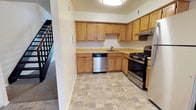 Located at 2002 Seldendale Dr in Hampton, Virginia, this two-story home offers a practical and well-organized layout across two levels. The kitchen is a standout feature, outfitted with warm honey-toned wood cabinetry that provides ample upper and lower storage. Stainless steel appliances include a gas range and a dishwasher, complemented by a double-basin sink and a light-toned countertop that ties the space together. The flooring features a neutral stone-patterned tile that is both durable and easy to maintain. A staircase visible from the kitchen connects the two floors, hinting at the vertical flow of the home's layout. The kitchen benefits from overhead lighting that keeps the workspace bright and functional. The overall design of the home reflects a straightforward, livable aesthetic with practical finishes throughout. The two-story structure allows for a natural separation between living and private spaces, making it a well-suited home for everyday comfort and functionality.