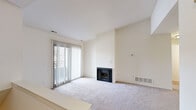 This single-floor unit offers a thoughtfully arranged layout encompassing a living room, kitchen, one bedroom, a walk-in closet, and a utility room. The living room serves as the central gathering space, finished with plush carpeting and neutral cream-toned walls that create a bright, open atmosphere. A fireplace anchors one wall, while large sliding glass doors fitted with vertical blinds flood the room with natural light and provide direct access to an outdoor balcony. A built-in niche adds a subtle architectural detail to the living area.

The kitchen is designed in a galley configuration, featuring dark granite countertops, warm honey-toned cabinetry, hardwood-style flooring, and stainless steel appliances including a refrigerator and range. A pass-through window connects the kitchen to the living area, enhancing the open feel. The bedroom is a comfortable, carpeted space with a natural light source through a window and convenient access to a spacious walk-in closet equipped with built-in shelving on both sides. A dedicated utility room provides additional functional storage, completing this efficiently organized unit.