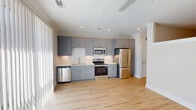 Located at 7630 Knightdale Boulevard in Knightdale, NC, this one-bedroom, one-bathroom unit offers a thoughtfully designed single-floor layout with contemporary finishes throughout. Light wood flooring runs continuously across the entire space, creating a warm, cohesive look that enhances the open feel of the floor plan.

The kitchen is a standout feature, outfitted with gray flat-front cabinetry, a white subway tile backsplash, and a full suite of stainless steel appliances including a refrigerator, electric range, microwave, and dishwasher. Recessed lighting and crown molding add a polished touch to this functional cooking area.

The living area benefits from large sliding glass doors covered by vertical blinds, allowing ample natural light to fill the room. A ceiling fan provides additional comfort, and the neutral wall tones complement the bright, airy atmosphere throughout.

The bedroom is generously proportioned and features a clerestory window that introduces additional light. A barn-style door leads to a walk-in closet, offering practical storage. The bathroom is finished with clean white subway tile surrounding a tub-shower combination, paired with a gray vanity and modern fixtures. The unit's overall design prioritizes clean lines, neutral palettes, and functional living in a compact yet comfortable space.