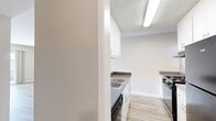 This single-floor, 3-bedroom, 1-bathroom residence in Vallejo, California offers a practical and well-organized layout with a clean, neutral aesthetic throughout. The combined kitchen and living room serves as the heart of the home, where a half-wall partition separates the two spaces while maintaining an open feel. The kitchen is equipped with white cabinetry, dark laminate countertops, a gas range, a refrigerator, and a single-basin sink, all illuminated by overhead fluorescent lighting and a textured ceiling. Light wood-style flooring runs throughout the main living areas, lending warmth and continuity to the space. The living room is bright and open, featuring a large sliding glass door that opens to a balcony with views of surrounding greenery, allowing ample natural light to fill the room. The primary bedroom is generously sized and includes a wide double closet with built-in shelving, carpeted flooring, and a window framing outdoor views. The additional bedrooms are similarly carpeted and provide natural light through windows. The bathroom includes a full soaking tub and shower combination in a clean white surround. Multiple hallways connect the rooms efficiently, and built-in shelving near the bathroom adds practical storage. Textured ceilings are consistent throughout the unit.