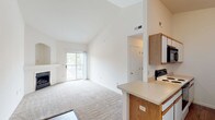 Located at 353 Autumn Creek Dr in Manchester, Missouri, this single-floor residence offers a thoughtfully designed layout with a clean, neutral palette throughout. The living area is a standout, featuring dramatic vaulted ceilings that amplify the sense of space and an elegant fireplace with an arched niche surround that serves as a natural focal point. Plush carpeting runs through the living and bedroom areas, while wood-style flooring defines the entryway and kitchen. A sliding glass door opens to a private balcony, inviting abundant natural light and outdoor views into the main living space. The galley-style kitchen is efficiently arranged with white cabinetry, oak-accented upper cabinets, light countertops, and a full suite of appliances including a range, microwave, dishwasher, and refrigerator. A peninsula counter provides a seamless transition to the living area. The bedrooms are carpeted and bright, with one featuring a sliding closet and a window overlooking the surrounding greenery. A hallway connects the private areas of the home, which include a bathroom with tile flooring and a soaking tub. Throughout, the space maintains a light, airy atmosphere complemented by high ceilings and a consistent, neutral color scheme.