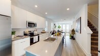 Located at 45 Boynton Ave SE in Atlanta, GA, this modern three-story home offers a thoughtfully designed layout across multiple levels. The main living floor showcases an open-concept floor plan where the kitchen flows seamlessly into the dining and living areas. The kitchen is outfitted with sleek white cabinetry, a subway tile backsplash, stainless steel appliances including a side-by-side refrigerator and electric range, and a generously sized island with quartz countertops and an undermount sink — ideal for both cooking and casual dining. Light wood-look flooring runs throughout the main level, complementing the bright, neutral color palette. The dining area benefits from natural light streaming through double windows with wood blinds, while the living room opens to a glass door, inviting additional light and outdoor access. The bedrooms are well-proportioned, featuring plush carpeting, ceiling fans, and ample window coverage. The primary bedroom connects directly to an en-suite bathroom equipped with a glass-enclosed walk-in shower finished in white subway tile. Additional bathrooms include a soaking tub with matching tile surround. The ground level houses a spacious garage with polished concrete floors and recessed lighting, offering generous storage or parking. This home combines clean architectural lines with modern finishes throughout.