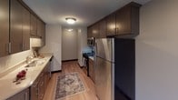 This single-floor space offers a thoughtfully designed layout that balances comfort and functionality. The kitchen is a standout feature, outfitted with dark espresso cabinetry, stainless steel appliances including a refrigerator, gas range, and microwave, as well as light countertops and warm hardwood-style flooring that lend a modern, welcoming feel. Ample upper and lower cabinet storage ensures practical use of the space.

The living and bedroom areas are finished with soft, neutral-toned carpeting and clean white walls accented by dark baseboards, creating a calm and versatile backdrop. A ceiling fan with integrated lighting in the bedroom adds both comfort and functionality, while a large sliding window frames views of lush surrounding trees, filling the room with natural light.

The bathroom is efficiently designed, featuring a tub-shower combination with a decorative curtain, dark overhead cabinetry for storage, and clean, neutral finishes throughout. The overall layout of the unit is open and practical, with natural light flowing in through multiple windows that overlook greenery, contributing to a bright and airy ambiance. Baseboard heating is present throughout, ensuring year-round comfort in this well-maintained space.