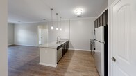 Located in Round Rock, Texas, this single-story, 5-bedroom, 2-bathroom home offers a well-designed open-concept layout that maximizes functionality. The kitchen serves as a central hub, featuring a granite-topped island with a stainless steel sink, dark cabinetry, a stainless steel dishwasher, and a refrigerator. Stylish pendant lights hang above the island, complementing the crown molding that frames the space. Wood-look hard flooring flows through the kitchen, living, and dining areas, creating a cohesive and easy-to-maintain aesthetic. The living room benefits from natural light through windows and a glass-paneled door. The dedicated dining room is anchored by an elegant multi-bulb chandelier and continues the warm flooring theme. The five bedrooms offer plush carpeting and ceiling fans, with the spacious primary bedroom providing generous room for furnishings. A well-appointed walk-in closet features wire shelving on three sides for ample storage. The bathrooms include a tub/shower combination with classic white subway tile surround and brushed nickel fixtures. Crown molding and neutral gray tones throughout lend a clean, modern ambiance to this thoughtfully designed home.