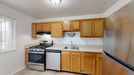 This single-floor residence offers a practical and comfortable layout designed for everyday living. The kitchen serves as a functional hub, featuring warm oak cabinetry — both upper and lower — paired with light-toned countertops. Stainless steel appliances include a gas range, dishwasher, and refrigerator, complemented by a built-in range hood and a stainless steel sink. The light hardwood-style flooring throughout the kitchen and main living areas lends a clean, cohesive aesthetic to the space.

The living area is bright and open, with light-toned walls, light hardwood-style flooring, and a window fitted with vertical blinds that allows natural light to fill the room. A partial wall divides the living space from the kitchen, creating a sense of separation while maintaining an open feel.

The bedrooms feature plush carpeting and neutral wall tones, providing a comfortable and quiet retreat. Each room includes closet access and windows with vertical blinds. One bedroom presents a tray ceiling detail, adding a subtle architectural element to the space.

The bathroom is clean and straightforward, offering a tub and shower combination, a toilet, and a wood-toned vanity with a countertop, all set on light hardwood-style flooring with a window providing natural ventilation and light.