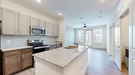 This single-floor residence offers a thoughtfully designed layout across two bedrooms and two bathrooms. The open-concept kitchen and living area serves as the heart of the home, where a granite-topped island with an integrated sink anchors the space. The kitchen is outfitted with stainless steel appliances, including a refrigerator, electric range, and over-the-range microwave, complemented by two-tone cabinetry featuring gray upper cabinets and warm wood-toned lower cabinets, set against a classic subway tile backsplash.

Light wood-style plank flooring extends throughout the main living areas, creating a cohesive and contemporary feel. The living room benefits from abundant natural light through large windows and a glass door that opens to an outdoor balcony, with a ceiling fan adding both function and style.

The primary bedroom features plush carpet flooring, a ceiling fan, direct access to one of the bathrooms, and a dedicated walk-in closet equipped with multi-tiered wire shelving for organized storage. The second bedroom is similarly carpeted and well-lit. Both bathrooms include wood-style flooring, a soaking tub with tiled surround, and clean, neutral finishes throughout.