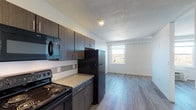 Located in Cincinnati, OH, this single-floor unit offers a thoughtfully designed open layout that seamlessly connects the kitchen and living areas. The kitchen is a functional centerpiece, outfitted with dark espresso-toned cabinetry, granite-style countertops, a subway tile backsplash, and a full suite of black appliances including an electric range, built-in microwave, dishwasher, and refrigerator. Wood-look plank flooring runs throughout the space, providing a warm, cohesive aesthetic that contrasts nicely with the clean white walls. The living area is bright and open, benefiting from a large multi-pane window that frames elevated views of the Cincinnati cityscape, with a wall-mounted HVAC unit positioned beneath. Recessed lighting in the entryway and kitchen adds to the well-lit atmosphere. The bathroom features large-format white wall tile, a vanity with granite-style countertop and dark cabinetry, and a separate tub and shower area. The entry foyer provides a clean transition into the main living space, with a dedicated electrical panel panel nearby. Overall, the unit presents a modern, updated interior with functional finishes and an efficient use of space.