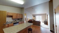 Located at 1455 Roughrider Blvd in Dickinson, North Dakota, this single-floor unit offers a practical and well-organized layout designed for comfortable everyday living. The open-concept kitchen and living area form the heart of the space, where warm hardwood flooring, vaulted ceilings, and natural light from a large sliding glass door create an inviting atmosphere. The kitchen is well-equipped with stainless steel appliances, including a range, microwave, and refrigerator, complemented by medium-toned wood cabinetry, laminate countertops, a central island with bar seating, and a dedicated pantry for additional storage. The living area flows naturally from the kitchen, featuring plush carpeting, generous seating space, and direct access to an outdoor balcony through the sliding glass door. The bedrooms are carpeted and offer a quiet, restful environment, with one room featuring its own wall-mounted air conditioning unit and a window with natural light. The bathroom is finished with tile flooring, a wood vanity, and well-lit mirror. A dedicated laundry room houses a full-size washer and dryer alongside overhead wire shelving, providing functional in-unit convenience throughout.