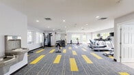 Located at 5865 Caribbean Blvd in West Palm Beach, Florida, this fitness center offers a well-appointed, single-floor workout facility designed to support a full range of exercise routines. The main workout area is spacious and open, featuring distinctive grey and yellow patterned carpet flooring that adds a bold, energetic aesthetic to the space. Recessed lighting throughout ensures consistent, bright illumination, while multiple large windows along the perimeter flood the room with natural light and offer views of the surrounding outdoors.

The cardio section is equipped with multiple treadmills, an elliptical trainer, a stationary bike, and a recumbent bike, each positioned near windows and wall-mounted flat-screen televisions for an engaging workout experience. On the opposite side, a full rack of dumbbells, a multi-function cable and strength machine, and an adjustable workout bench provide ample options for strength and resistance training. A large wall mirror in the free weights area enhances the sense of space and allows for proper form checks.

An integrated water fountain station is conveniently located within the facility, and a clean, tiled restroom with natural light is available on-site. The fitness center also connects directly to adjacent community amenities, making it a central hub for an active lifestyle.