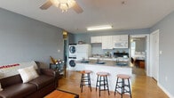 This single-floor unit offers a thoughtfully designed open-concept layout that seamlessly connects the living room, dining area, and kitchen. The living room features warm hardwood flooring, a ceiling fan, and a window that allows natural light to fill the space. The kitchen is outfitted with white cabinetry, a full suite of appliances including a refrigerator, electric range, and built-in microwave, as well as a granite-topped peninsula with bar seating for three — ideal for casual dining and entertaining. A stacked washer and dryer unit is conveniently integrated into the main living area, adding practical in-unit laundry access. The first bedroom is carpeted and equipped with a ceiling fan, a closet, and ample space for furnishings. The second bedroom also features carpet flooring and is brightened by a window with natural light. Two bathrooms serve the unit: one includes a walk-in shower with a glass enclosure and a single vanity with white cabinetry, while the second features a full bathtub and shower combination alongside a vanity with storage. Cool blue-gray tones carry throughout the unit, creating a calm and cohesive aesthetic. The overall layout is efficient and functional, making it well-suited for comfortable day-to-day living.