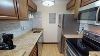 This single-floor studio is thoughtfully designed to maximize functionality within an open, efficient layout. The galley-style kitchen is a standout feature, showcasing warm wood cabinetry, granite countertops, and a striking mosaic stone tile backsplash. Stainless steel appliances — including a refrigerator, dishwasher, electric range, and microwave — provide a modern, cohesive look. Light wood-style flooring runs throughout the kitchen and into the main living area, creating visual continuity. A breakfast bar with bar stools offers a convenient casual dining option adjacent to the kitchen.

The open main living area comfortably accommodates a sleeping space and a sitting area side by side, with warm hardwood flooring, neutral walls, and a large window dressed with vertical blinds that allows natural light to filter in. A wall-mounted HVAC unit provides climate control directly within the room.

The bathroom is clean and functional, featuring light tile flooring, a granite-topped vanity with a white basin sink, a full tub with shower, and a large mirror that enhances the sense of space. Overall, the unit offers a practical and comfortable living environment with updated finishes throughout.