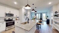 This thoughtfully designed single-floor residence showcases a contemporary open-concept layout that seamlessly connects the kitchen, dining, and living areas. The kitchen serves as a central focal point, featuring a large granite-topped island with an undermount sink and matte black faucet, white shaker-style cabinetry, classic subway tile backsplash, and stainless steel appliances including a side-by-side refrigerator. Three pendant lights with industrial-style black shades illuminate the island, adding a stylish contrast to the bright, white cabinetry. Wood-look flooring runs throughout the main living areas, lending warmth and continuity to the space.

The living room is bright and inviting, benefiting from multiple windows and a glass door that opens to a private balcony, allowing generous natural light to fill the room. The bedrooms are carpeted for comfort, each offering multiple windows with outdoor views and ceiling fans. Walk-in closets with wire shelving systems provide practical storage solutions. The bathroom features clean white subway tile surrounding the tub and shower, paired with a granite-topped vanity and wood-look flooring, creating a crisp, modern aesthetic throughout.