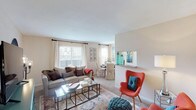 This single-floor residence offers a thoughtfully organized layout across one bedroom and one bathroom. The living area serves as the heart of the home, featuring neutral-toned carpet, warm beige walls, and large windows that invite natural light while offering views of the outdoor surroundings. The open feel of the space is enhanced by a pass-through opening that connects the living area to the kitchen, promoting a sense of connectivity throughout.

The galley-style kitchen is efficiently designed with white cabinetry lining both sides, laminate countertops, a double-basin stainless steel sink, and white appliances including a range and refrigerator. Stone-patterned vinyl flooring adds durability and contrast to the bright cabinetry.

The bedroom is generously sized, featuring soft carpeting, a ceiling fan with light fixture, and a window that provides natural light. A wide sliding-door closet offers ample storage space. The room comfortably accommodates a full-sized bed and additional furnishings.

The bathroom is accessible via a carpeted hallway and features a single-sink vanity with storage cabinetry below, a large mirror with overhead lighting, and a clean, functional layout. Additional doors along the hallway provide further storage options.