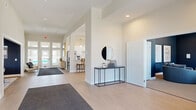 Located at 8935 Thornton Hall Blvd in Reynoldsburg, Ohio, this single-floor community space offers a well-appointed and versatile layout designed to accommodate a variety of social and functional needs. The welcoming entryway features light hardwood-style flooring, clean white walls, and a stylish console table with a round mirror, setting a polished, modern tone throughout.

The kitchen is a standout feature, offering an expansive galley-style layout with crisp white cabinetry, stainless steel appliances, white quartz countertops, and a row of elegant brass pendant lights overhead. A bar-height counter with wood-and-cane seating provides a casual gathering spot adjacent to the kitchen, making it ideal for entertaining.

The living areas are diverse in character. A bright lounge features deep navy walls, large windows that flood the space with natural light, and curated artwork, creating a sophisticated yet comfortable retreat. A separate media room continues the navy palette and is equipped with a wall-mounted television, curved sectional seating, and a popcorn machine — perfect for movie screenings or group gatherings.

A dedicated meeting room with a round wood table, plush seating, and floor plan displays offers a professional setting for presentations or consultations. Additionally, a carpeted flex room with a bold textured accent wall provides a creative and versatile space. Throughout, the design balances contemporary style with functional comfort.