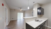 Located at 2395 N Forest Rd in Getzville, NY, this well-appointed 2-bedroom, 3-bathroom single-floor residence offers a thoughtfully designed layout with modern finishes throughout. The open-concept living, dining, and kitchen area serves as the heart of the home, featuring rich hardwood-style flooring, a ceiling fan, and a sliding glass door that floods the space with natural light. The kitchen is outfitted with dark cabinetry, crisp white countertops, a peninsula with pendant lighting, and a full suite of stainless steel appliances including a gas range, microwave, and refrigerator. A hallway with a pendant light fixture connects the main living area to the private quarters, where two carpeted bedrooms provide comfortable retreats. The generously sized primary bedroom includes a walk-in closet with wire shelving and an en-suite bathroom. An additional closet and bathroom are accessible from the hallway. All three bathrooms feature hardwood-style flooring and clean, neutral finishes, with at least one offering a full soaking tub with shower. A dedicated in-unit laundry room accommodates a full-size washer and dryer with overhead shelving for added storage. Neutral gray tones and white trim carry throughout, lending the space a cohesive, contemporary aesthetic.