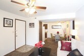 This single-floor unit offers a practical and well-organized layout, with distinct areas for living, dining, cooking, sleeping, and bathing. The living room serves as the central gathering space, featuring plush carpeting, a ceiling fan with light fixture, and a sliding glass door fitted with vertical blinds that allows natural light to fill the room while providing access to an outdoor area. Adjacent to the living room, the dining area accommodates a round table and chairs beneath another ceiling fan, with chair-rail molding lining the walls for a subtle decorative touch.

The galley-style kitchen is efficiently designed with dark wood cabinetry on both sides, laminate countertops, a double-basin stainless steel sink, and white appliances including a refrigerator, electric range, and dishwasher. Light tile flooring runs throughout the kitchen and continues into the bathroom, which features a dark wood vanity with a white countertop, a toilet, and tile flooring.

The bedroom is a calm, carpeted space with a window that brings in natural light, textured ceiling, and ample room for furnishings. Throughout the unit, textured ceilings and neutral wall tones contribute to a clean, understated ambiance.