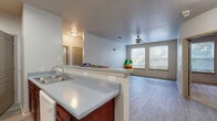 Located at 2145 Candler Rd in Decatur, GA, this single-floor residence offers two bedrooms, two full bathrooms, and two closets within a well-organized layout. The combined kitchen and living room area is anchored by a peninsula-style pass-through counter that opens toward the main living space, creating a connected and functional flow. The kitchen features rich mahogany-toned cabinetry, light countertops, wood-look vinyl flooring, and a full suite of white appliances including a refrigerator, electric range, and sink. The living area extends from the kitchen with the same durable flooring and benefits from ceiling-mounted lighting. Both bedrooms are carpeted and include ceiling fans, with the primary bedroom offering notable space and dual windows that bring in natural light and outdoor views. The second bedroom is also carpeted and well-sized. Both bathrooms share a consistent design, each featuring a single-sink vanity with mahogany cabinetry, light countertops, a tub/shower combo with white tile surround, and matching wood-look flooring. Two dedicated closets provide practical storage throughout the residence. The overall aesthetic is clean and neutral, with warm wood tones and light walls creating a cohesive, understated character throughout.