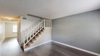 Located at 4860 Brookhaven Rd in Macon, Georgia, this two-story, 2-bedroom, 2-bathroom unit is distributed across two floors, with the larger main level and a secondary upper level. The main floor features durable hardwood-style flooring throughout the living area and kitchen. The kitchen is equipped with white cabinetry, granite-style countertops, a black refrigerator, electric range, and dishwasher, with an adjacent dining or utility area providing additional space. A carpeted staircase with a white railing connects the main level to the upper floor. Both bedrooms are carpeted and feature ceiling fans with light fixtures, neutral gray walls, and closets. The primary bedroom includes a window with natural light and an open closet with shelving. The second bedroom also features a window and a standard closet. Two bathrooms serve the unit — one full bathroom with a tub/shower combo, white vanity, and dark wood-style flooring, and a second bathroom with similar finishes. Textured ceilings are present throughout. The overall aesthetic is clean and neutral, offering a functional and straightforward layout suited for comfortable everyday living.