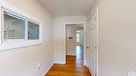 This single-story community facility offers a thoughtfully organized layout across six distinct areas, all unified by warm honey-toned hardwood flooring and crisp white walls that create a clean, welcoming atmosphere throughout.

The spacious lounge area serves as the heart of the space, featuring an open layout with recessed lighting and natural light streaming in through windows. Comfortable seating arrangements — including patterned accent chairs, a gray sofa, and a coffee table — are complemented by decorative wall art, giving the area a relaxed yet polished feel. A media console with a flat-screen television adds a practical entertainment element.

Adjacent to the lounge, a dedicated computer business center provides workstations along a built-in desk, equipped with multiple computers, keyboards, and a printer. A window overlooking greenery brings in natural light, making it a functional and pleasant workspace.

The laundry facility is well-equipped with multiple front-loading washer and dryer units arranged in a row, offering ample capacity for shared use. The room maintains the same consistent flooring and neutral wall tones found throughout the space.

Connecting hallways with white six-panel doors and windowed walls tie the rooms together seamlessly. The overall design is practical and community-focused, with consistent finishes and a comfortable, approachable ambiance throughout.