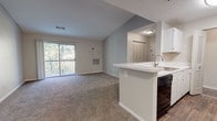 Located at Town Brooke in Middletown, Connecticut, this single-floor residence offers a well-organized, open-concept layout designed for comfortable everyday living. The living area is carpeted and bathed in natural light through a sliding glass door that leads to a private balcony overlooking a lush, wooded backdrop—providing a tranquil, nature-filled setting. The space transitions seamlessly into the kitchen, which features a peninsula with a built-in sink and white cabinetry, complemented by wood-style flooring and black appliances including a refrigerator, range, and dishwasher. A dedicated hallway connects the living area to the private quarters of the unit. The bedroom is generously proportioned, with plush carpeting and a large window framing views of the surrounding trees. A spacious walk-in closet with wire shelving provides ample storage. The bathroom is finished with wood-style flooring, a white vanity, and a tiled tub-and-shower combination accented with a neutral tile border detail. Throughout the unit, neutral wall tones, textured ceilings, and consistent finishes contribute to a clean, cohesive aesthetic.
