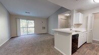 Located at Town Brooke in Middletown, Connecticut, this single-floor residence offers a well-organized, open-concept layout designed for comfortable everyday living. The living area is carpeted and bathed in natural light through a sliding glass door that leads to a private balcony overlooking a lush, wooded backdrop—providing a tranquil, nature-filled setting. The space transitions seamlessly into the kitchen, which features a peninsula with a built-in sink and white cabinetry, complemented by wood-style flooring and black appliances including a refrigerator, range, and dishwasher. A dedicated hallway connects the living area to the private quarters of the unit. The bedroom is generously proportioned, with plush carpeting and a large window framing views of the surrounding trees. A spacious walk-in closet with wire shelving provides ample storage. The bathroom is finished with wood-style flooring, a white vanity, and a tiled tub-and-shower combination accented with a neutral tile border detail. Throughout the unit, neutral wall tones, textured ceilings, and consistent finishes contribute to a clean, cohesive aesthetic.