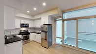 Located at 1818 State Street in San Diego, this contemporary single-floor residence offers a thoughtfully designed layout with clean, modern finishes throughout. The kitchen is a standout feature, boasting crisp white cabinetry with sleek hardware, dark countertops, and a classic subway tile backsplash. Stainless steel appliances — including a gas range, over-the-range microwave, and full-size refrigerator — provide both style and functionality. Light hardwood-style flooring runs throughout, contributing to a warm yet modern aesthetic. Large floor-to-ceiling windows and a glass-paneled door flood the space with natural light, creating an open, airy atmosphere while offering views of the surrounding area. Recessed lighting adds a polished finishing touch to the interior. The overall design reflects a balance of practicality and contemporary style, making it a well-suited space for modern urban living in one of San Diego's vibrant neighborhoods.