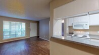 Located at 11444 Vance Jackson Rd in San Antonio, Texas, this single-floor residence offers a well-organized layout with a comfortable mix of living, dining, and private spaces. The open living area welcomes natural light through a large front window fitted with blinds, and is finished with rich wood-look flooring that extends throughout the main living spaces, creating a warm and cohesive aesthetic. A textured ceiling adds character throughout the unit.

The kitchen is accessible via a pass-through counter with granite-look laminate surfaces, providing a convenient connection to the living area. White cabinetry lines the walls, offering ample storage, while white appliances — including a coil-burner electric range, over-the-range microwave, and refrigerator — complete the functional cooking space. Light wood-look flooring continues here, maintaining a consistent feel.

The bedrooms are carpeted for comfort and include windows that bring in natural light. At least one bedroom features a walk-in closet, providing generous storage. The unit includes two full bathrooms, each appointed with a single-sink vanity featuring granite-look countertops, white cabinetry, wood-look flooring, and a tiled tub/shower combination — offering practical, clean finishes throughout.