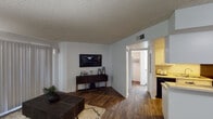 This single-floor residence offers a thoughtfully designed layout that maximizes functionality and flow throughout its key living spaces. The living room serves as the central gathering area, featuring dark hardwood-style flooring, a textured ceiling, and a large sliding glass door dressed with vertical blinds that allows ample natural light to fill the room. The open layout connects seamlessly to the dining area, which is equipped with a ceiling fan and is positioned adjacent to the kitchen for convenient everyday living. The kitchen features a pass-through counter design with white cabinetry, a sink, and dark appliances, making it both practical and visually connected to the dining space. Built-in shelving on the kitchen partition adds additional storage and display opportunities. The bedroom is a standout space, highlighted by a rich, dark wood shiplap accent wall that adds warmth and a bold design statement. Carpeted flooring, a window with vertical blinds for natural light and privacy, and ample space for furnishings make it a comfortable retreat. A closet and bathroom are accessible from the hallway connecting the living area to the bedroom, completing the functional layout of this well-organized single-story residence.