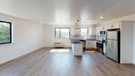 Located at 6774 Ridge Ave in Philadelphia's Roxborough neighborhood, this single-floor unit showcases a thoughtfully designed open-concept layout with modern finishes throughout. Warm hardwood-style flooring flows continuously across the living and kitchen areas, creating a cohesive and inviting atmosphere filled with natural light from multiple black-framed windows that frame neighborhood and treetop views.

The kitchen is a standout feature, equipped with white shaker-style cabinetry accented by matte black hardware, dark granite countertops, and a classic white subway tile backsplash. A peninsula with pendant lighting provides additional prep space and defines the transition between the kitchen and open living area. Stainless steel appliances, including a range, built-in microwave, refrigerator, and dishwasher, complete the space. Recessed lighting and pendant fixtures add functional illumination throughout.

The living area is generously proportioned, with clean white walls and natural light streaming in from multiple windows. Additional rooms provide flexible living space, each featuring hardwood-style flooring, recessed lighting, and windows with exterior views. A well-appointed entryway with multiple closets offers convenient storage. The bathroom features marble-style tile surrounding a soaking tub and shower combination, a dark vanity with marble countertop, and tile flooring, lending a refined, spa-like quality to the space.
