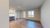 North Grove A1D (Unit 15-204) is a thoughtfully designed 2-bedroom, 1-bathroom apartment spanning 690 square feet in Riverside, CA 92501. The single-floor layout maximizes functionality while offering a clean, contemporary aesthetic throughout.

The kitchen is a standout feature, showcasing a two-tone cabinetry design with white upper shaker-style cabinets and slate-blue lower cabinets, complemented by a white subway tile backsplash and dark countertops. Stainless steel appliances — including a French door refrigerator, range, microwave, and dishwasher — complete this well-appointed space, all set atop light hardwood-style flooring with recessed lighting above.

The primary bedroom measures 120 square feet and, like the secondary bedroom, features neutral carpet flooring and light-toned walls. Both bedrooms benefit from natural light, with the primary offering a large window with views of the surrounding community. The secondary bedroom provides a bright, versatile space with clean white walls.

The bathroom mirrors the kitchen's design language with matching slate-blue cabinetry, a wide vanity with integrated sink, large mirror, and a full shower-tub combo, all finished with the same warm hardwood-style flooring.

A connecting hallway ties the unit together efficiently. The community exterior features modern stucco architecture and covered solar parking structures.