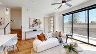 This contemporary two-story home in Phoenix, AZ offers a thoughtfully designed layout spread across two floors, including 2 bedrooms, 3 bathrooms, a dedicated office, and generous closet storage. The main level features a bright, open living area with light hardwood flooring, recessed lighting, a ceiling fan, and large black-framed sliding glass doors that open to an outdoor balcony, filling the space with natural light. The kitchen is a standout, boasting dual-tone cabinetry with white upper cabinets and warm wood-grain lowers, a crisp white quartz waterfall island with an undermount sink, a full white tile backsplash, and stainless steel appliances. The dedicated office includes hardwood floors, a ceiling fan, and a window with outdoor views. Upstairs, the spacious primary bedroom features floor-to-ceiling black-framed windows, a ceiling fan, wood flooring, and a walk-in closet. The second bedroom is equally well-appointed with its own ceiling fan and access to a closet. The bathrooms are elegantly finished with wood-tone floating vanities, white quartz countertops, and stone tile flooring — one featuring a frameless glass walk-in shower with black fixtures and a window. The overall aesthetic is clean, modern, and cohesive throughout.