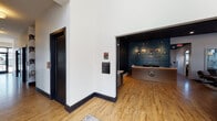 This single-story community clubhouse in Huber Heights, Ohio, is thoughtfully designed with a contemporary aesthetic that blends industrial and farmhouse-inspired elements throughout. Warm hardwood flooring runs continuously across the space, complemented by bold black trim, doors, and accents that create striking visual contrast against crisp white walls.

The entrance welcomes visitors with soaring ceilings, decorative industrial gear wall art, and a comfortable built-in seating nook alongside an inviting reception desk area framed by a deep teal accent wall adorned with a curated photo display. A well-lit hallway with barn-style sliding doors connects the various areas of the clubhouse.

The lounge area is a standout feature, anchored by a shiplap fireplace wall with a rustic wood mantle, wall-mounted television, and ample seating. Clerestory windows invite generous natural light. Adjacent to the lounge is a game area featuring a wooden shuffleboard table and casual seating.

A spacious gathering room opens dramatically through a full glass overhead garage door, flooding the interior with outdoor views and natural light. A large communal dining table provides an ideal setting for group events.

The bar area features a quartz waterfall island with seating, gray cabinetry with gold hardware, a shiplap accent wall with decorative shelving, and beverage refrigerators. A dedicated refreshment station with a commercial coffee machine and wine cooler completes the amenities.