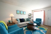 Located at 2100 Westminster Ln in Virginia Beach, Virginia, this single-floor residence offers a well-organized layout with multiple bedrooms, a living area, a functional kitchen, and a full bathroom. The living room is a welcoming space featuring tile and carpet flooring, a large window dressed with sheer curtains that invite natural light, and clean white walls that lend a bright, open feel. The kitchen is efficiently designed in a galley style, outfitted with warm wood cabinetry, dark granite-style countertops, black appliances including a gas range and dishwasher, and tile flooring, with a windowed door providing additional light and exterior access. The bedrooms are carpeted and well-sized, each featuring closet storage. One bedroom includes a walk-in style closet and direct access to an adjoining room, while another offers a dedicated workspace area alongside natural light from a window with teal curtains. The full bathroom features tile flooring, a wood vanity with granite-style countertops, a mirror, and a tub-shower combination. Throughout the residence, the neutral color palette and consistent finishes create a cohesive and comfortable living environment suited for everyday living.