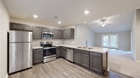 Located at 6400 Birch Trail Ln. in Columbus, Ohio, this single-floor home offers a well-designed layout with modern finishes throughout. The kitchen serves as a standout feature, equipped with stainless steel appliances including a range, microwave, and dishwasher, all complemented by rich gray shaker-style cabinetry and light granite countertops. Light wood-look flooring runs throughout the kitchen and entry areas, lending a clean, contemporary feel. The kitchen opens toward the living area, which boasts vaulted ceilings with a ceiling fan, creating an airy, open atmosphere with a view to the outdoors through a sliding door. The bedrooms are carpeted for comfort and include ceiling fans and windows that bring in natural light. The bathroom features elegant marble-look tile flooring, a dark-toned vanity with a white countertop, and a glass-enclosed shower. A dedicated laundry room includes washer and dryer hookups, wire shelving, and matching wood-look flooring. The attached garage is drywalled and includes an electrical panel, offering functional utility space. Overall, the home presents a clean, move-in-ready environment with thoughtful design details and practical amenities throughout.