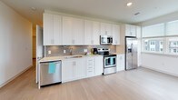 This single-floor residence offers a clean, contemporary design throughout its well-organized layout. The kitchen serves as a functional centerpiece, featuring floor-to-ceiling white shaker cabinetry, light quartz countertops, and a gray subway tile backsplash. Stainless steel appliances — including a refrigerator with ice maker, electric range, over-the-range microwave, and dishwasher — complement the light wood-style flooring that extends through the main living areas.

The bedrooms are finished with plush neutral carpet and ceiling fans, contributing to a comfortable, quiet atmosphere. Large windows fitted with horizontal blinds allow natural light to fill the rooms while offering views of the surrounding cityscape. The bathroom is well-appointed with a wide white vanity, dual sinks, a large mirror with backlit fixtures, ample drawer storage, and a glass-enclosed walk-in shower. Light wood-tone flooring carries through the bathroom, reinforcing the cohesive aesthetic of the space.

Overall, the residence maintains a bright, neutral palette with modern finishes throughout, creating a clean and functional living environment.